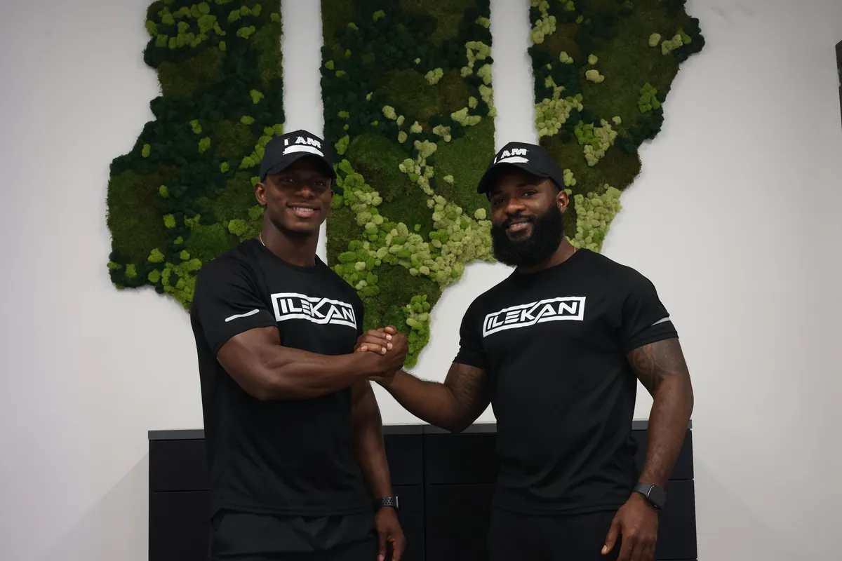 Brothers Tunde and Tolu clasping hands in front of the club's moss wall